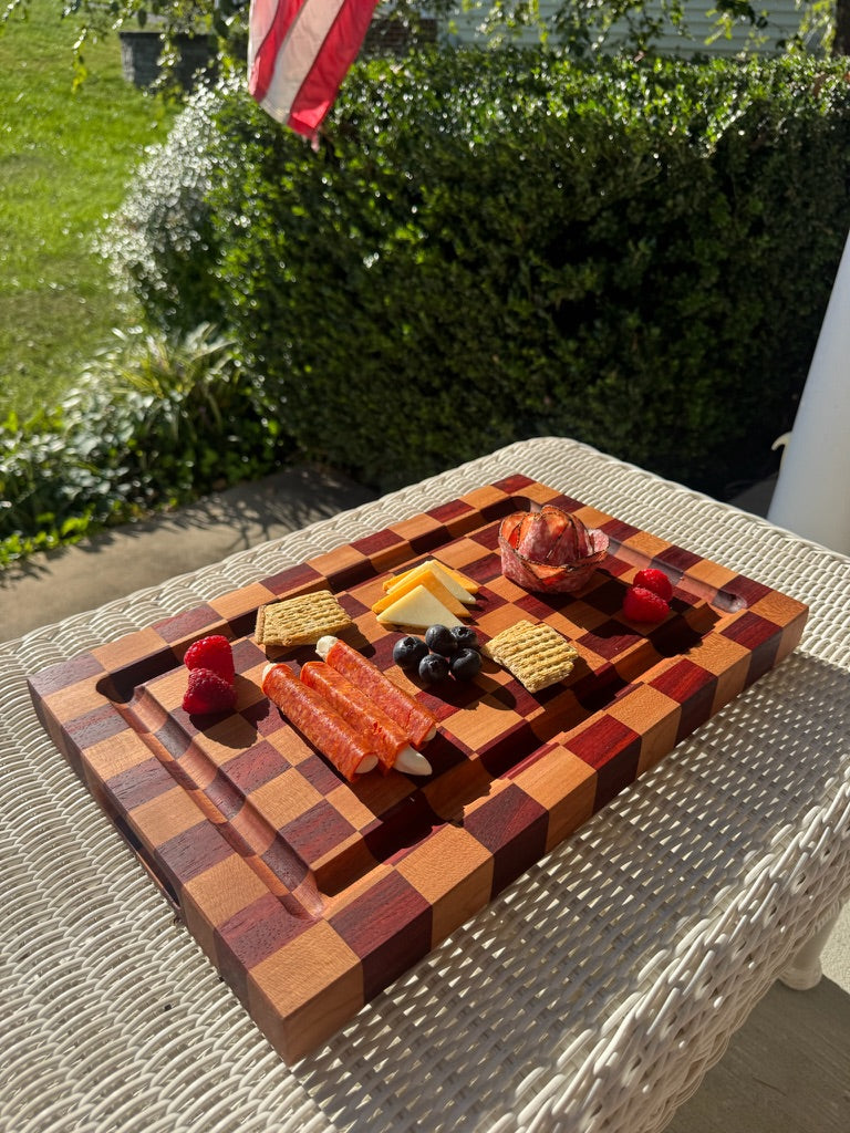 Wooden charcuterie board with assorted meats, cheeses, and fruits on a patio table.