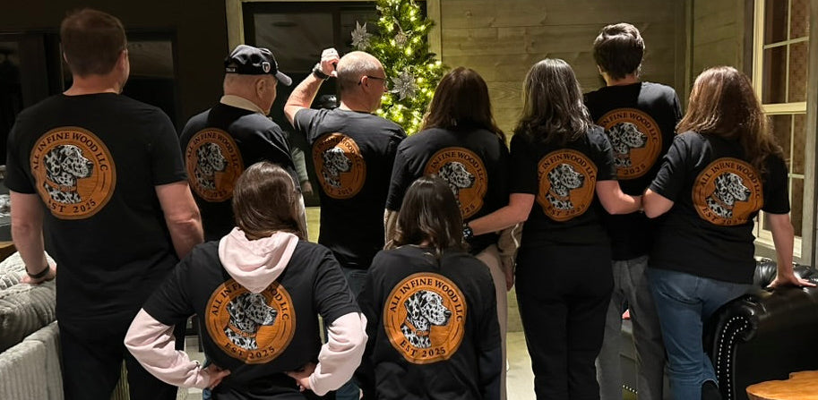 Group of people wearing black t-shirts with a logo on the back in a room with wooden walls and a Christmas tree.