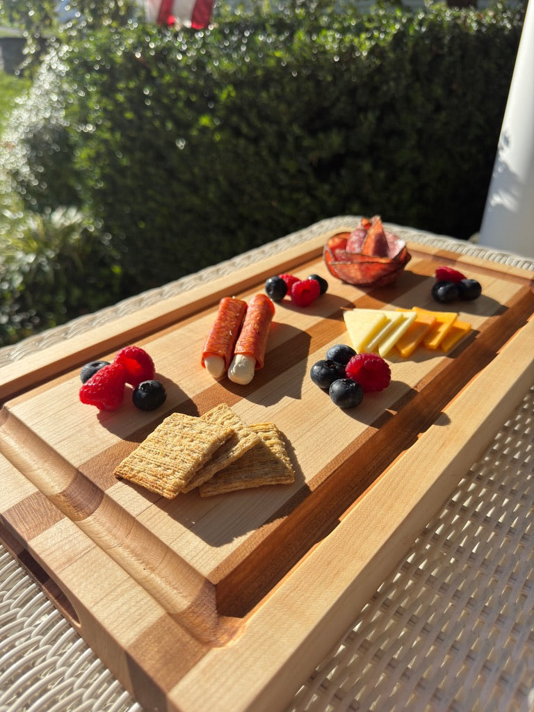Wooden charcuterie board with cheese, crackers, and fruits on a blurred outdoor background