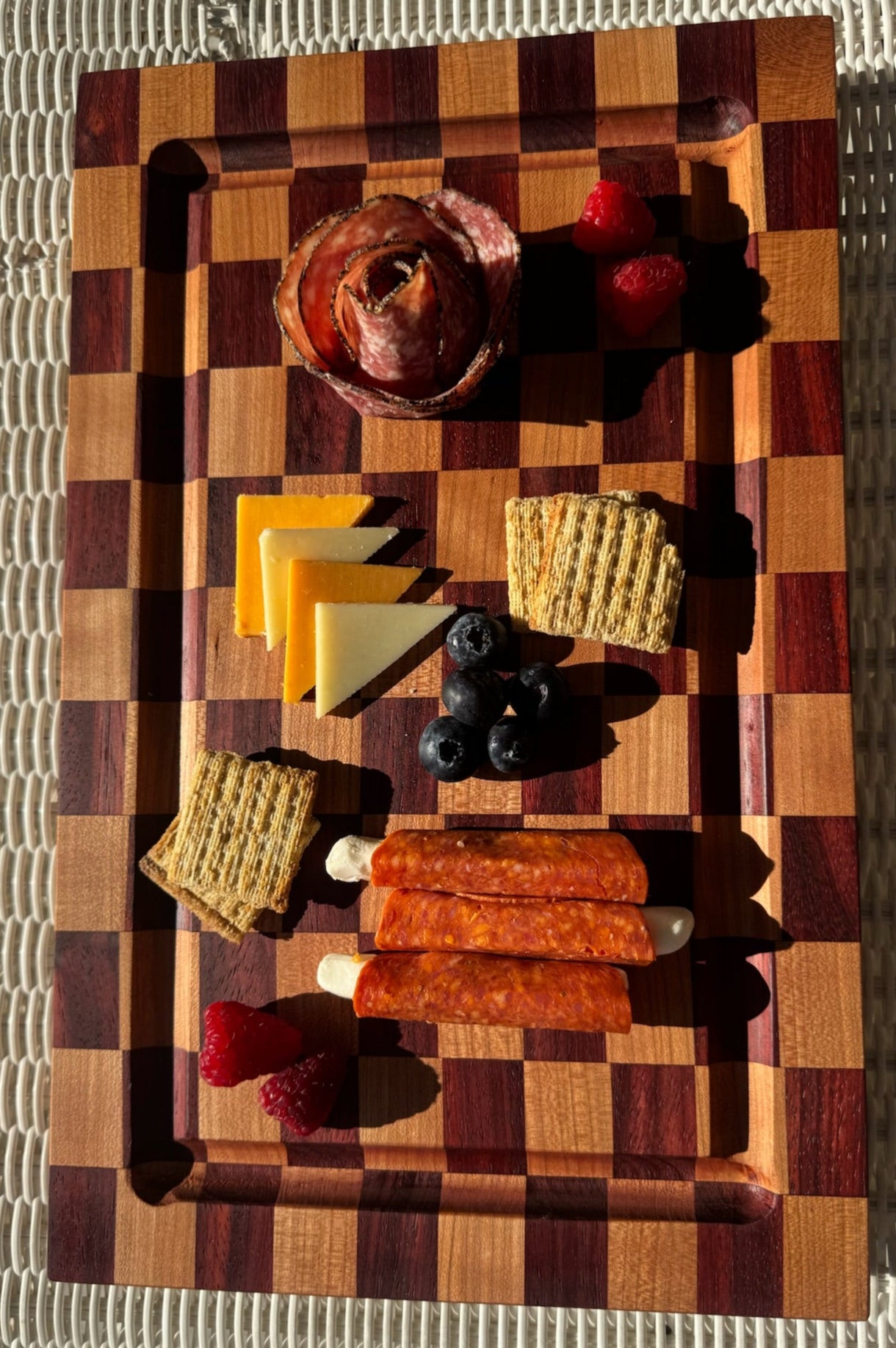 Wooden cutting board with assorted meats, cheeses, and fruits on a textured surface