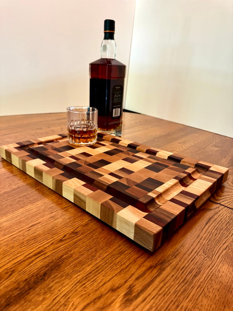 Wooden cutting board with geometric pattern on a wooden surface, accompanied by a bottle of Bourbon and a glass.