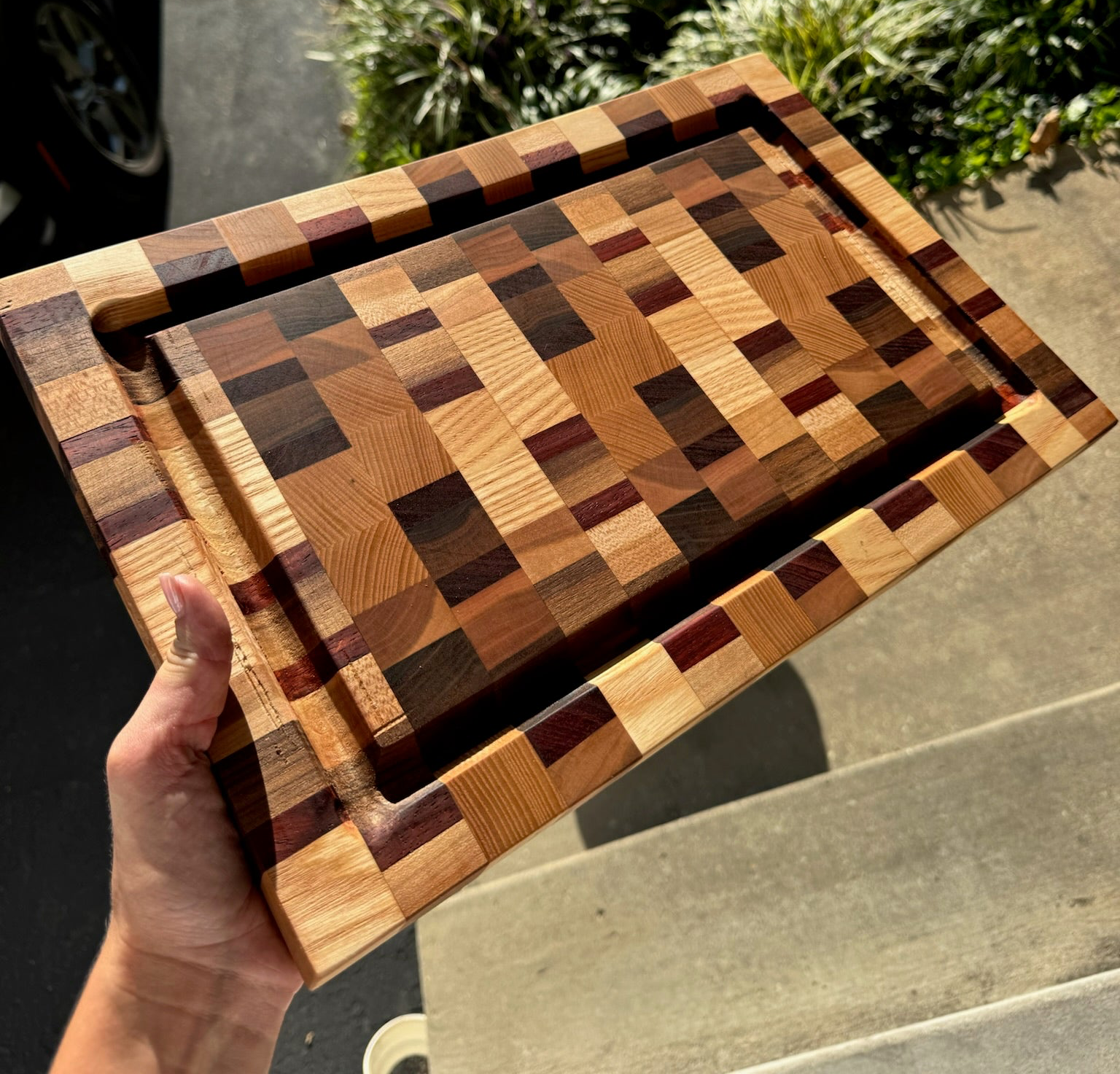 Hand holding a wooden cutting board with a geometric pattern on a concrete surface.