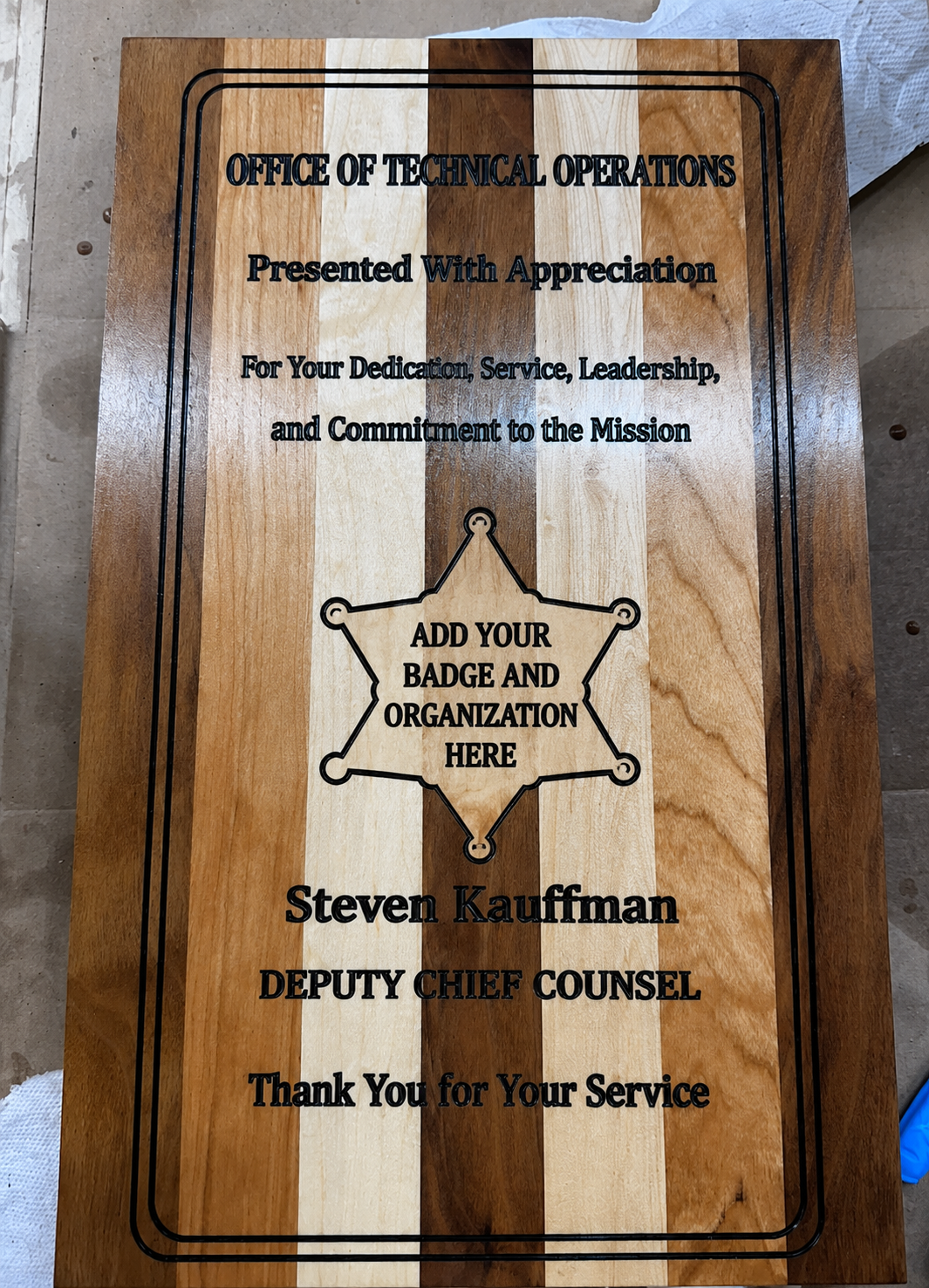 Wooden plaque with engraved text and a  your department badge.