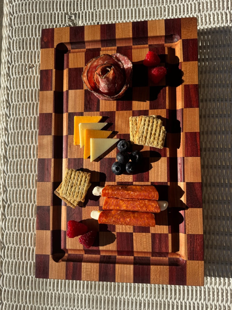 Wooden cutting board with assorted meats, cheeses, and fruits on a textured surface